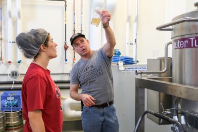 A professor talks with a student while examining a glass of beer