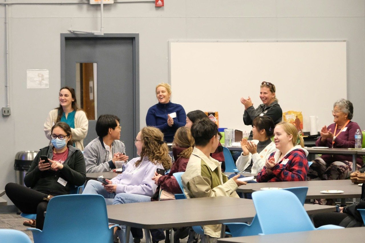 An audience in a classroom claps for a speaker.