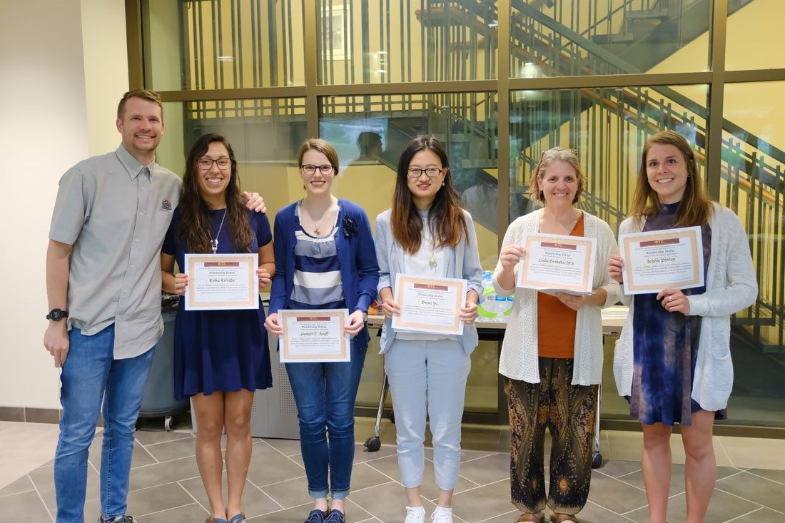 Group of students receiving certificates with professor standing next to them